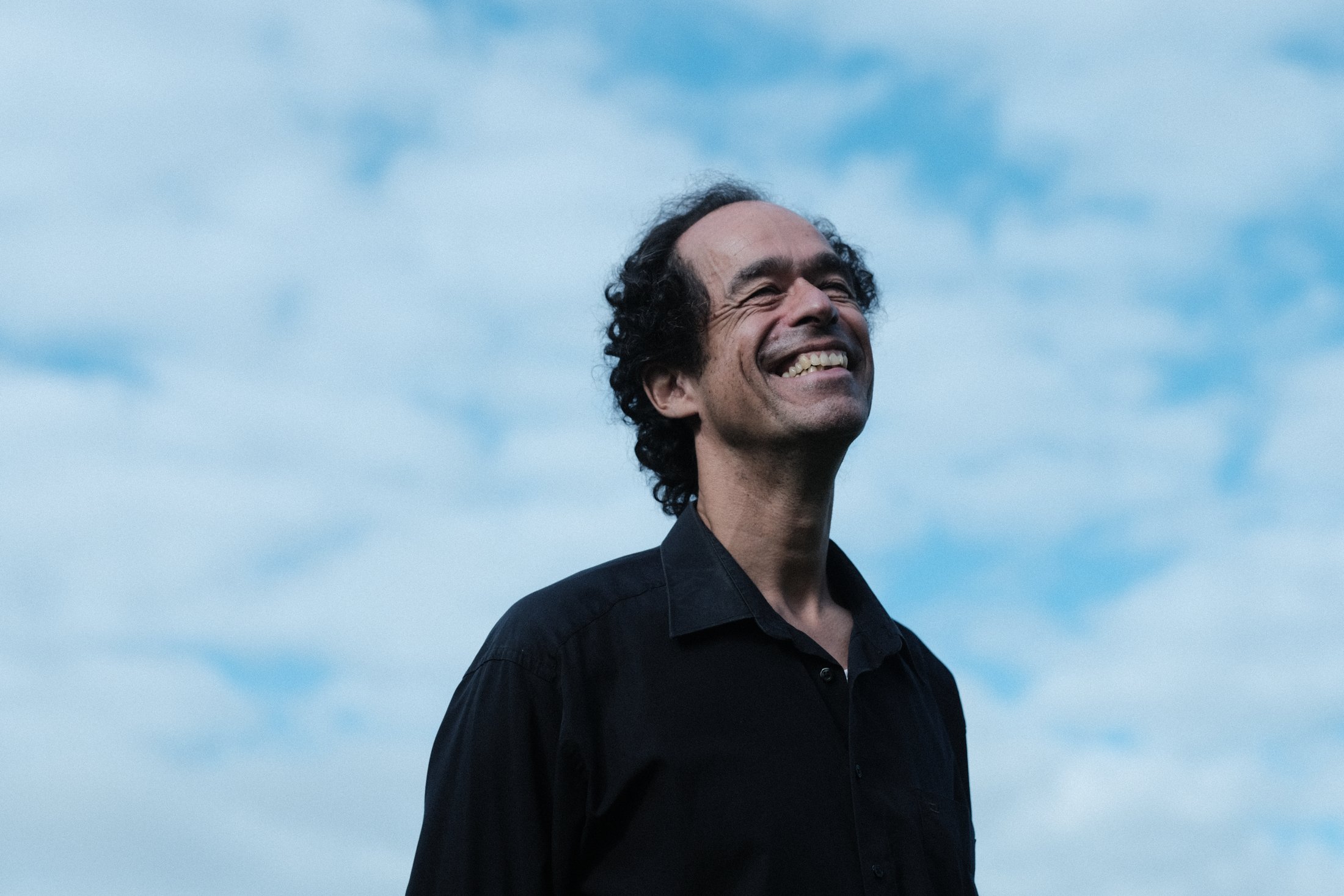 Jérôme Inen smiling broadly against a bright blue sky with clouds
